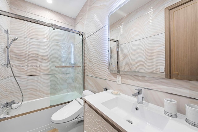 full bathroom featuring backsplash, toilet, shower / bath combination with glass door, vanity, and tile walls