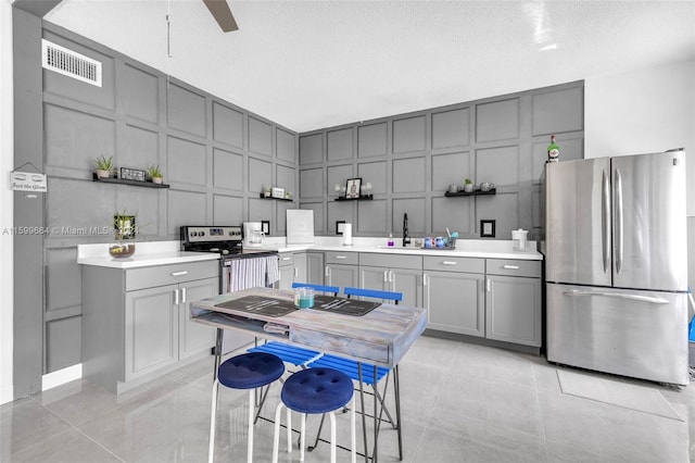 kitchen with a textured ceiling, stainless steel appliances, gray cabinets, and ceiling fan