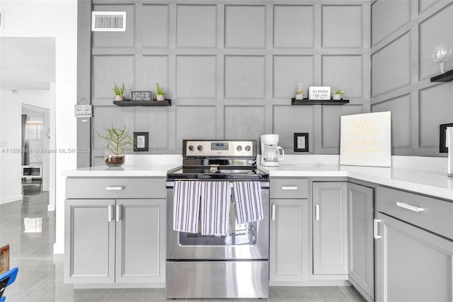 kitchen featuring light tile patterned floors, light stone counters, electric stove, and gray cabinets