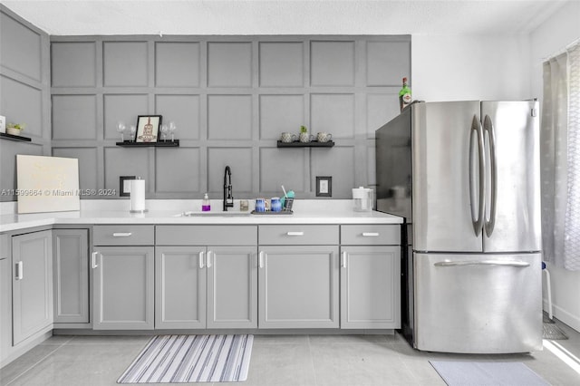 kitchen featuring gray cabinetry, light tile patterned floors, stainless steel refrigerator, and sink