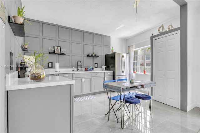 kitchen with gray cabinets, stainless steel fridge, sink, and a textured ceiling