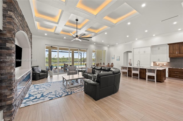 living room with beam ceiling, ceiling fan, coffered ceiling, light hardwood / wood-style floors, and ornamental molding