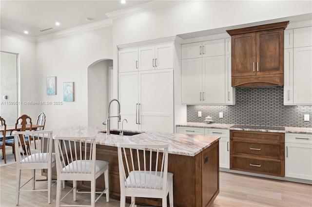 kitchen with tasteful backsplash, white cabinetry, an island with sink, sink, and stovetop