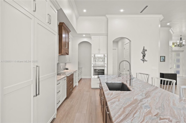 kitchen featuring sink, white cabinetry, light hardwood / wood-style flooring, stainless steel double oven, and light stone countertops