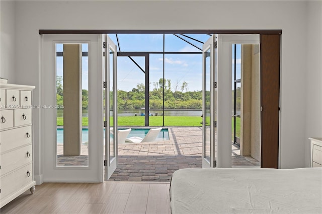 bedroom featuring light wood-type flooring, access to outside, and a water view