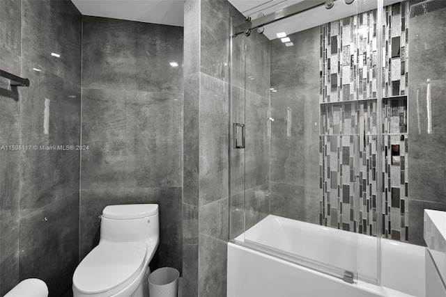 bathroom featuring combined bath / shower with glass door, tile walls, and toilet