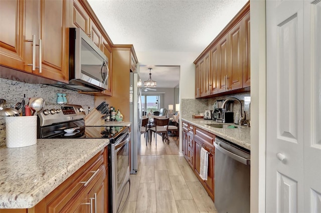 kitchen featuring pendant lighting, stainless steel appliances, light stone countertops, and sink