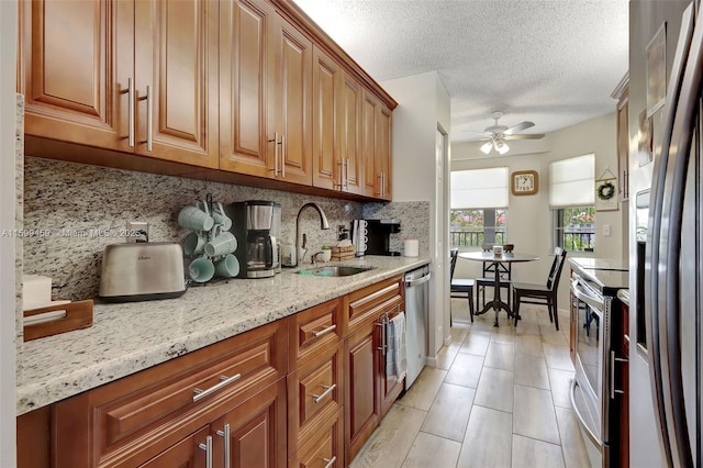 kitchen featuring sink, backsplash, ceiling fan, stainless steel appliances, and light stone countertops