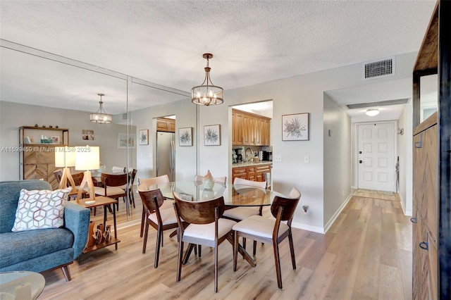 dining room featuring a notable chandelier, sink, a textured ceiling, and light wood-type flooring