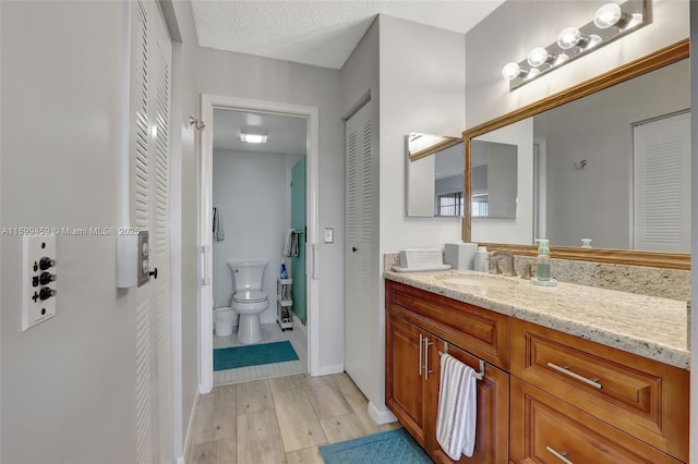 bathroom featuring vanity, a textured ceiling, wood-type flooring, and toilet