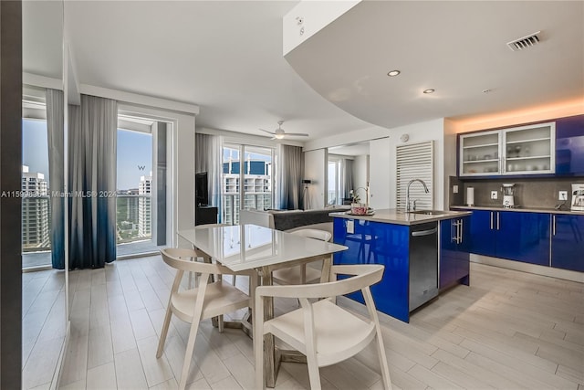 kitchen featuring a center island with sink, blue cabinets, sink, ceiling fan, and a kitchen bar