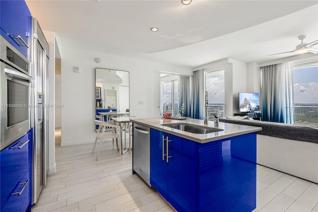 kitchen featuring ceiling fan, blue cabinets, a kitchen island with sink, and sink