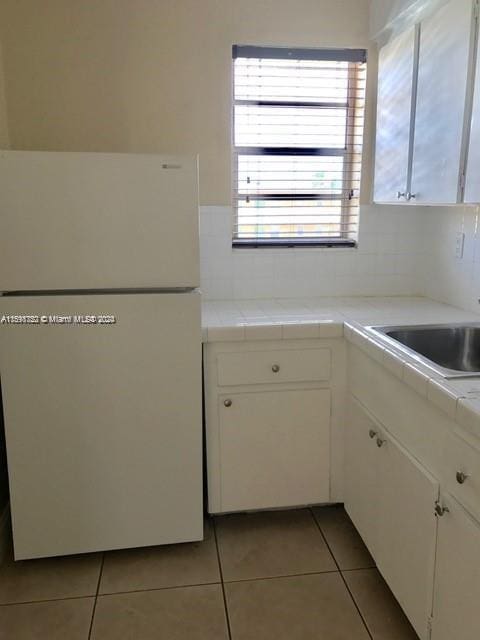 kitchen featuring light tile patterned floors, tile countertops, white fridge, and white cabinetry