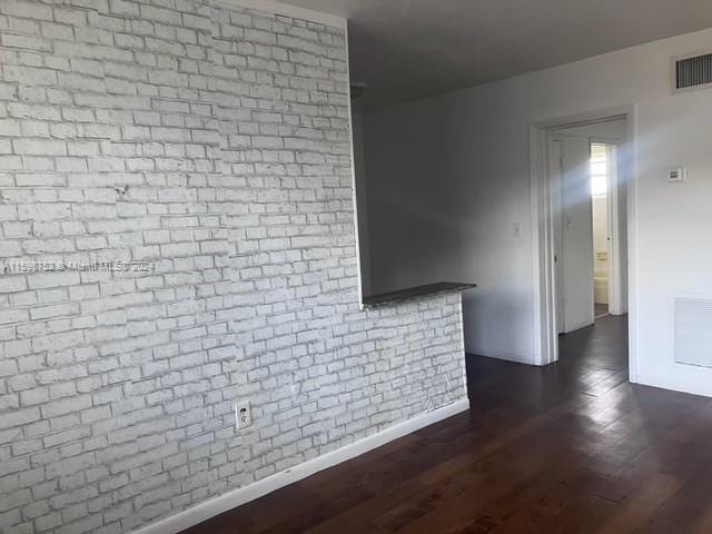 unfurnished living room featuring brick wall and dark hardwood / wood-style flooring