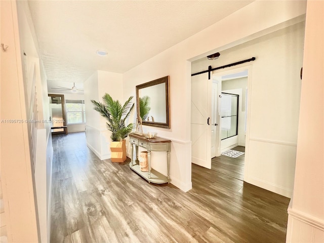 hallway with a barn door, hardwood / wood-style flooring, and a textured ceiling