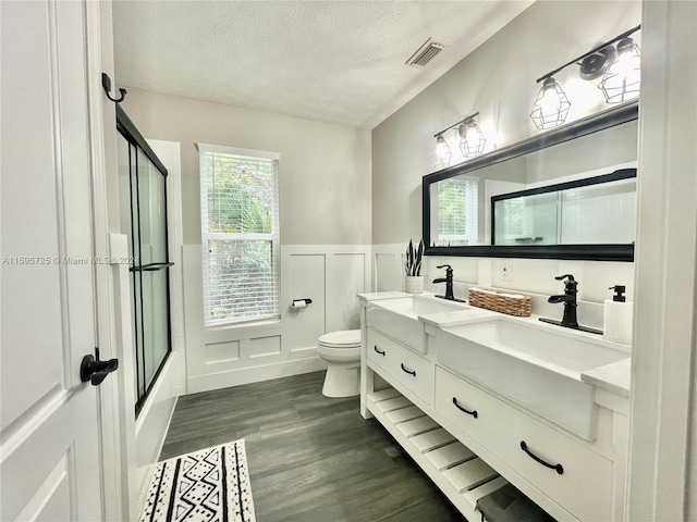 full bathroom with a textured ceiling, double sink, hardwood / wood-style floors, vanity with extensive cabinet space, and toilet