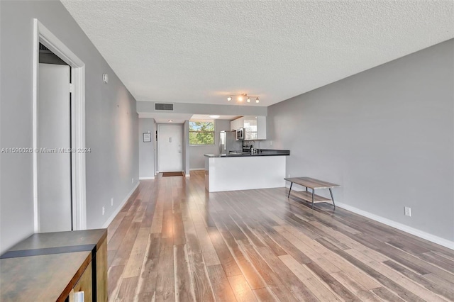 kitchen with white cabinetry, a textured ceiling, kitchen peninsula, wood-type flooring, and track lighting