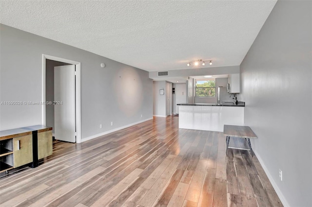 empty room with a textured ceiling, track lighting, and light wood-type flooring