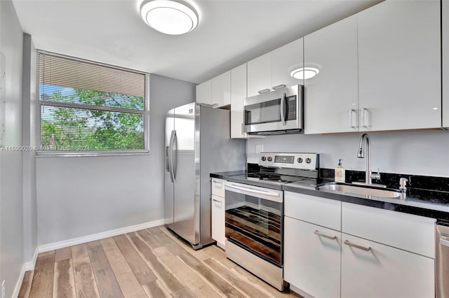 kitchen with appliances with stainless steel finishes, light hardwood / wood-style floors, sink, and white cabinets