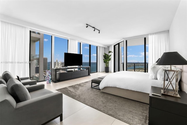 tiled bedroom featuring expansive windows, access to outside, track lighting, and a water view