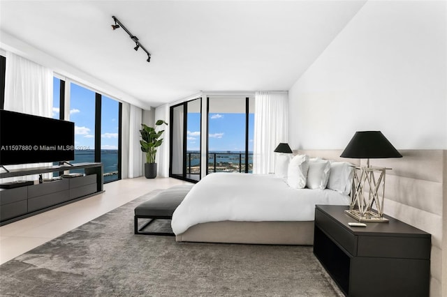 bedroom with light tile floors, access to exterior, a water view, and rail lighting