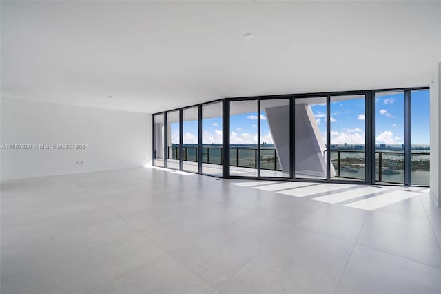 tiled empty room featuring a healthy amount of sunlight, a water view, and a wall of windows