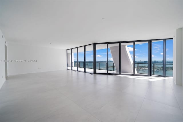 tiled empty room featuring a wealth of natural light, a water view, and floor to ceiling windows