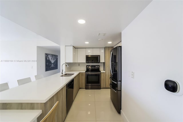 kitchen featuring appliances with stainless steel finishes, a kitchen bar, sink, white cabinets, and light tile patterned floors