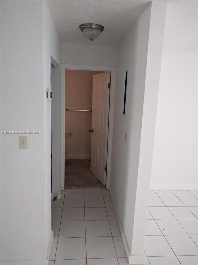 corridor featuring a textured ceiling and light tile patterned floors