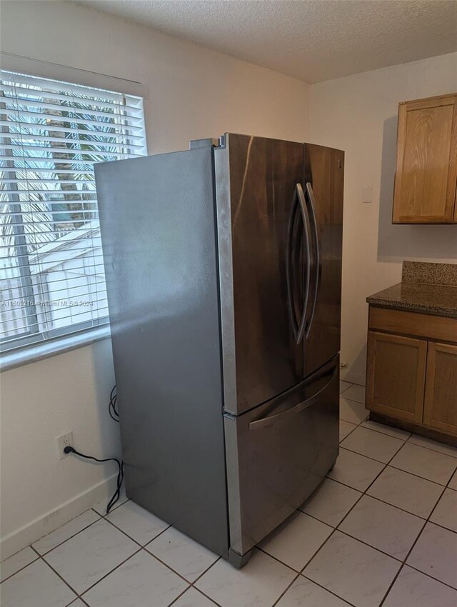 kitchen with stainless steel refrigerator, a textured ceiling, and light tile patterned floors