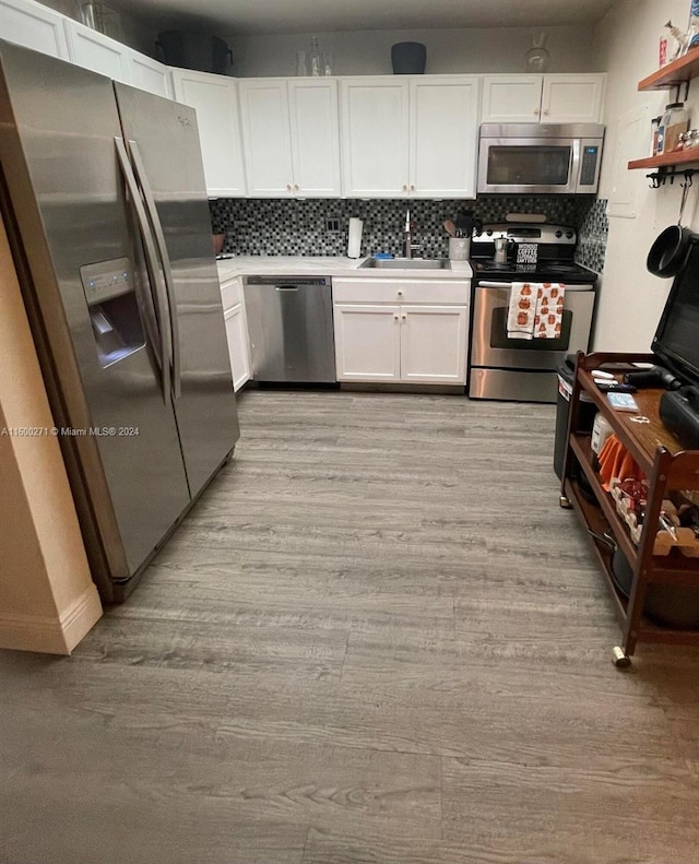 kitchen with light hardwood / wood-style flooring, decorative backsplash, white cabinets, and stainless steel appliances