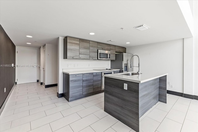 kitchen with dark brown cabinetry, stainless steel appliances, sink, light tile patterned floors, and a center island with sink