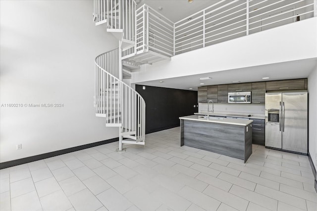 kitchen with dark brown cabinetry, a center island with sink, a towering ceiling, and stainless steel appliances