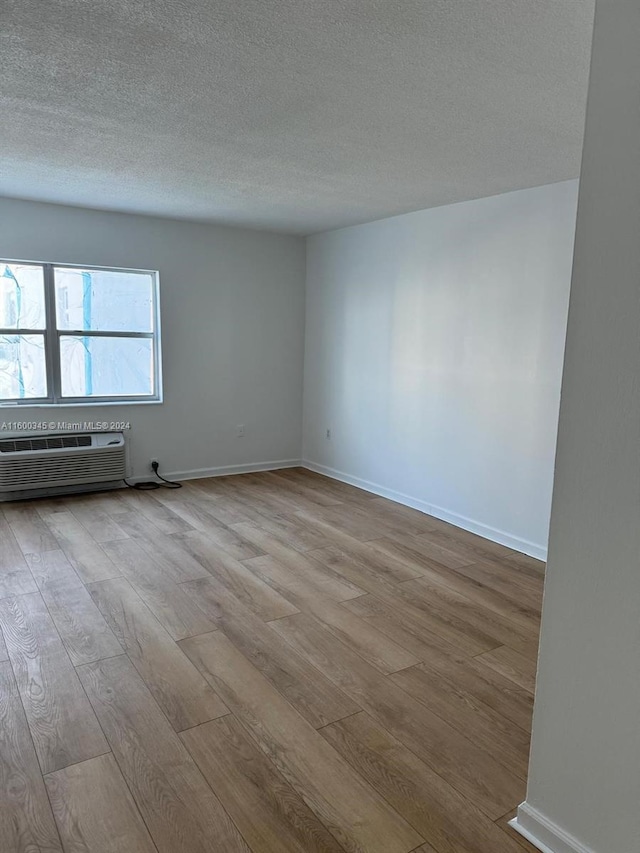 unfurnished room featuring a wall unit AC, a textured ceiling, and light hardwood / wood-style flooring