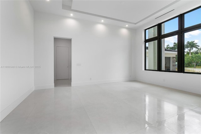 unfurnished room with recessed lighting, baseboards, a high ceiling, and a tray ceiling