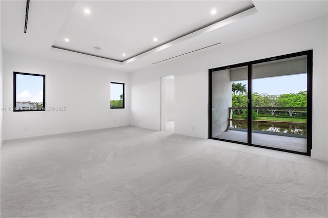 spare room with recessed lighting, a tray ceiling, light colored carpet, and a healthy amount of sunlight