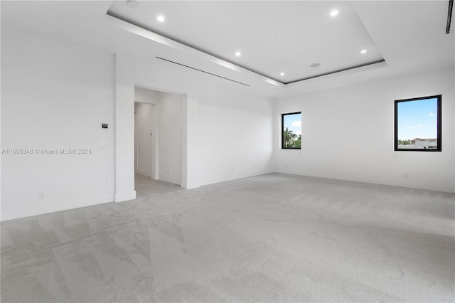 spare room featuring a raised ceiling, recessed lighting, and light carpet