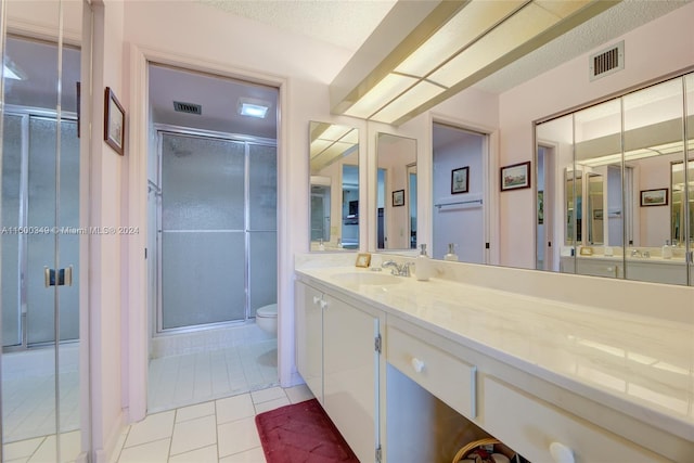 bathroom with tile flooring, a textured ceiling, a shower with shower door, toilet, and large vanity