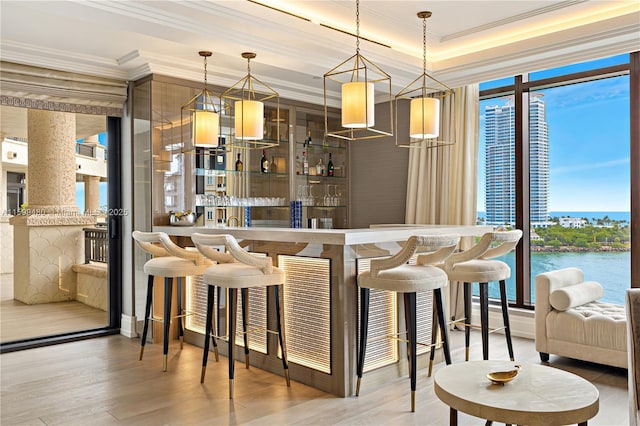 bar with wood-type flooring, a water view, pendant lighting, and crown molding