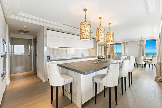 kitchen featuring a center island, light hardwood / wood-style floors, decorative light fixtures, a breakfast bar area, and white cabinets