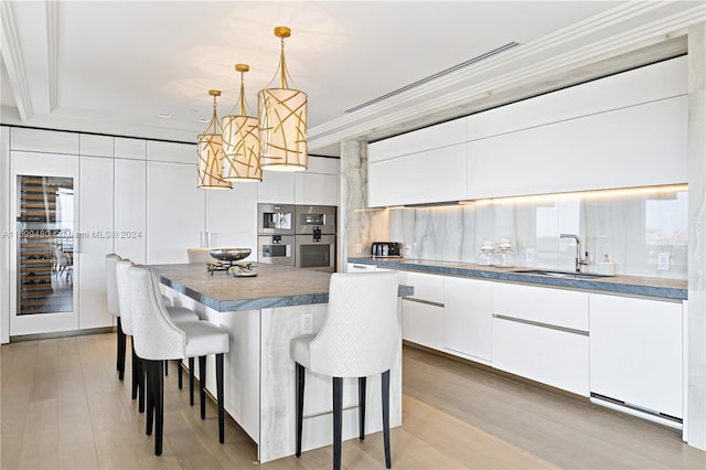 kitchen with sink, light hardwood / wood-style floors, pendant lighting, white cabinets, and ornamental molding