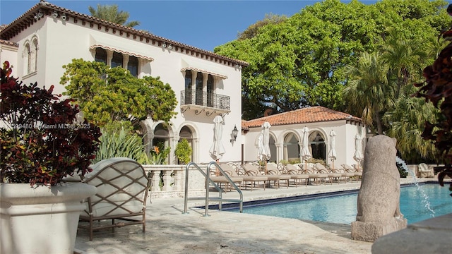 rear view of house featuring a balcony, a patio, a community pool, a tile roof, and stucco siding