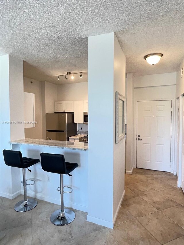 kitchen featuring kitchen peninsula, stainless steel appliances, white cabinetry, track lighting, and a breakfast bar