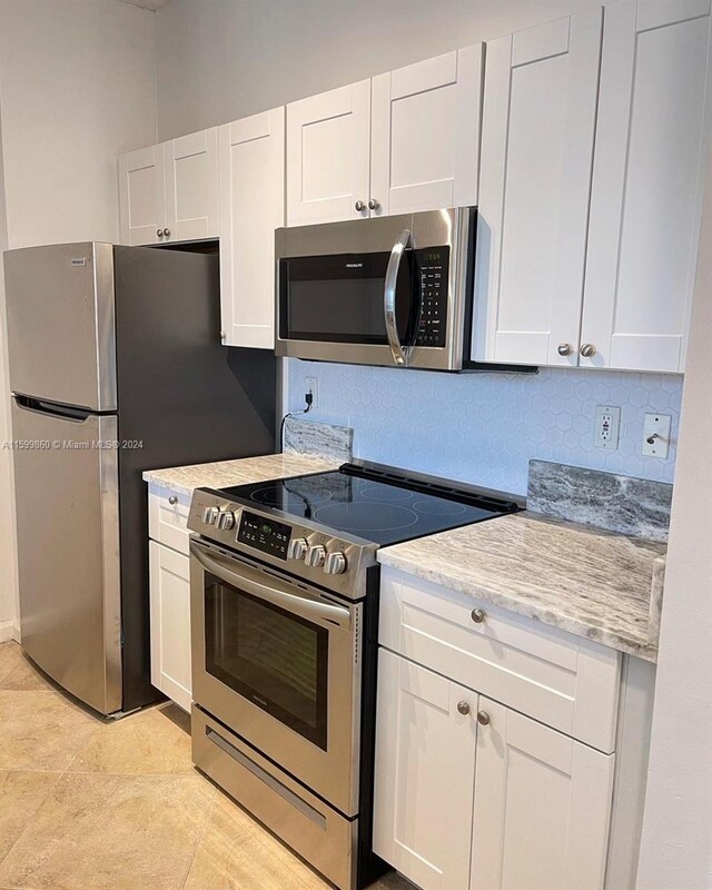 kitchen with light stone countertops, tasteful backsplash, stainless steel appliances, light tile flooring, and white cabinetry