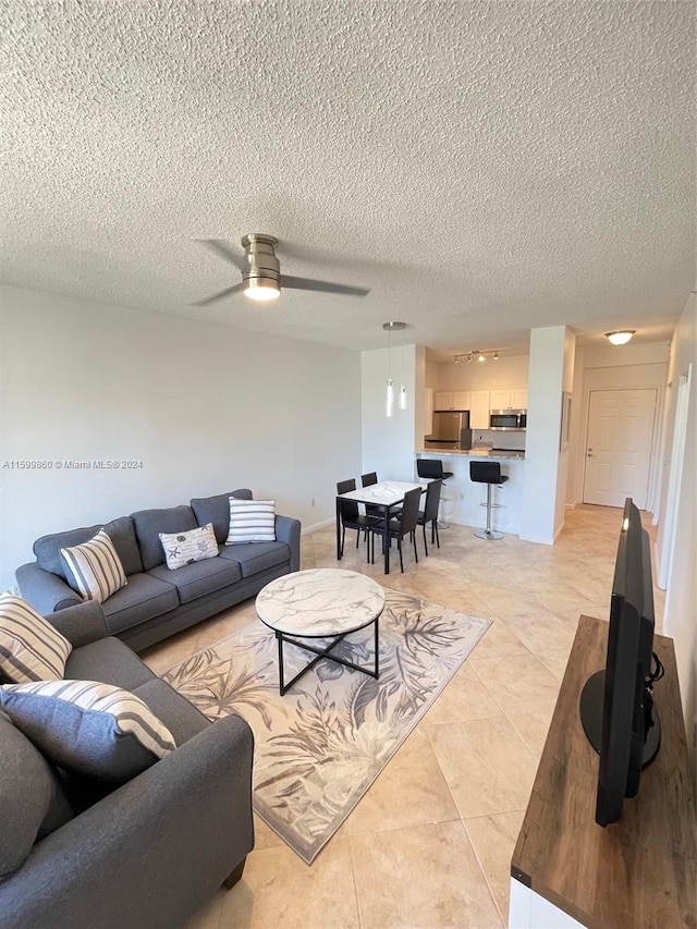 living room with a textured ceiling, light tile flooring, and ceiling fan