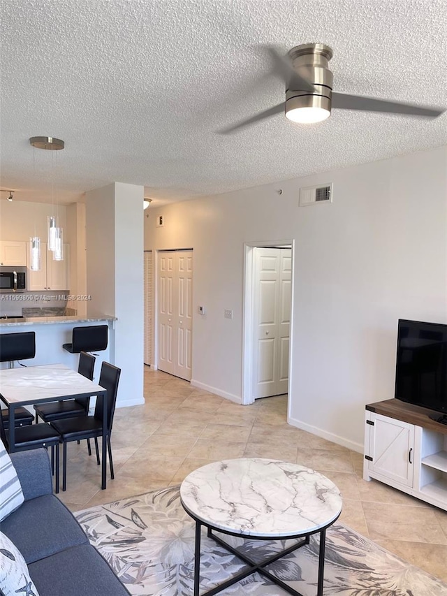 living room with a textured ceiling, ceiling fan, and light tile floors