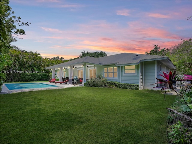 back of property at dusk featuring a patio area, metal roof, an outdoor pool, and a lawn