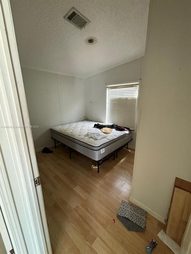 bedroom with visible vents, a textured ceiling, baseboards, and wood finished floors