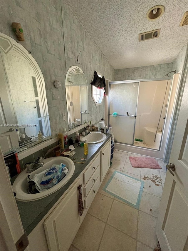 bathroom with a textured ceiling, a shower stall, visible vents, and a sink