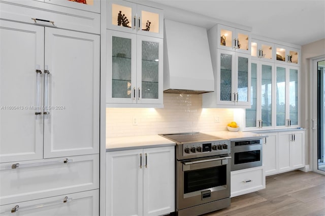 kitchen featuring light hardwood / wood-style floors, tasteful backsplash, white cabinets, appliances with stainless steel finishes, and premium range hood